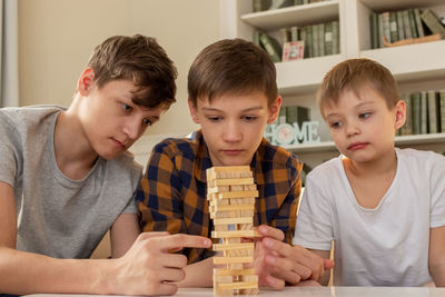 Three boy are playing a board game made of wooden rectangular blocks