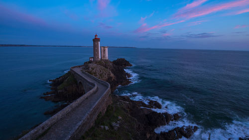 Lighthouse amidst sea and buildings against sky