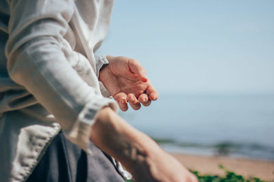 Midsection of man holding hands at beach against sky