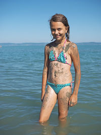 Happy young woman standing in sea against clear sky