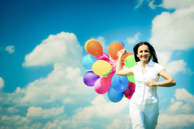 Low angle view of woman holding balloons against sky