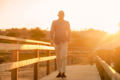 Full length of man standing by railing during sunset