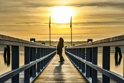 Silhouette woman walking on footbridge against sky during sunset