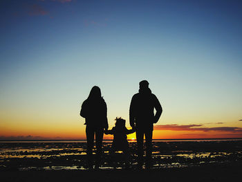 Silhouette people on beach against sky during sunset