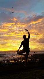 Full length of woman practicing yoga at beach against sky during sunset