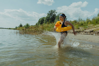 Girl running through water with inflatable yellow duck at the lake on sunny day