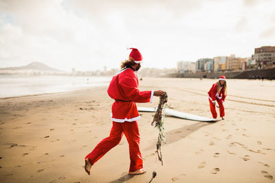 Couple wearing santa costumes at beach against sky