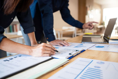 Midsection of businesswoman and colleague working on table