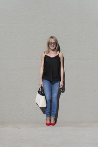 Portrait of smiling young woman standing against wall