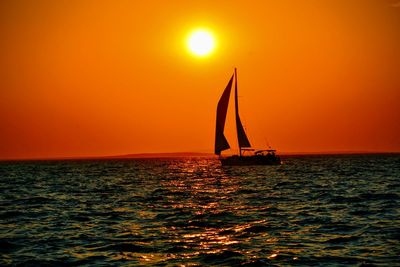 Silhouette sailboat sailing on sea against orange sky