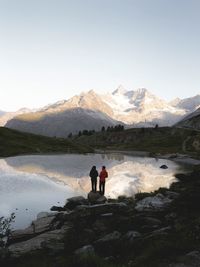 People standing on mountain by lake against clear sky