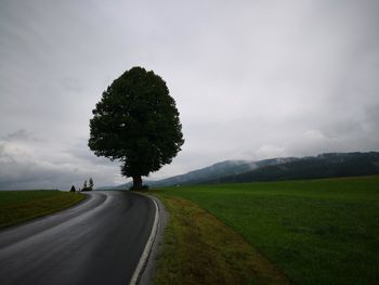 Road amidst trees on field against sky