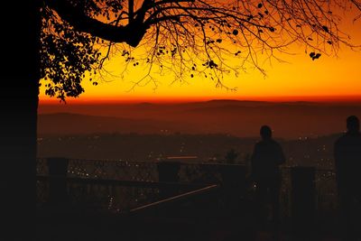 Silhouette people standing by sea against orange sky