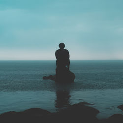 Silhouette man sitting by sea against sky