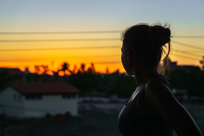 Side view of woman standing on field against sky during sunset