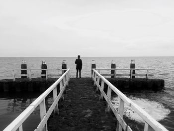 Rear view of man standing on rock by sea against clear sky