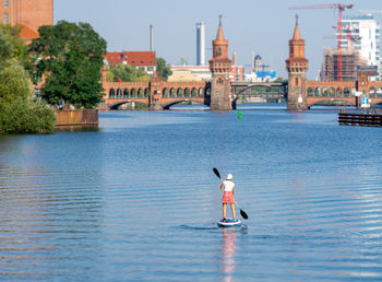 Rear view of man in river against sky in city