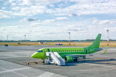 Modern green civil passenger aircraft parked on airfield. a ladder is docked to the plane. 