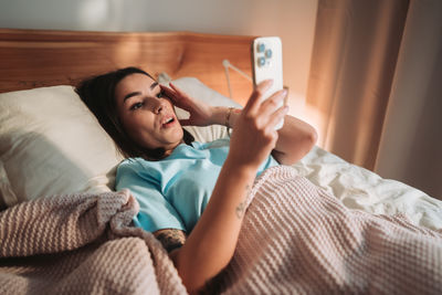 Young woman using mobile phone on bed at home