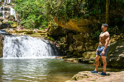Full length of shirtless man standing in waterfall