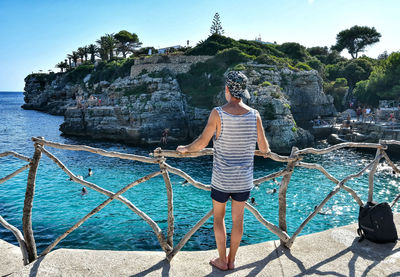 Man standing on rock by sea against sky