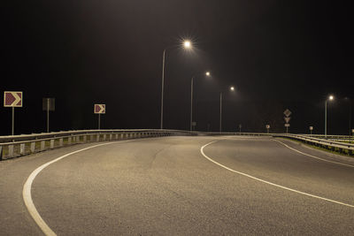 Empty road along illuminated street lights