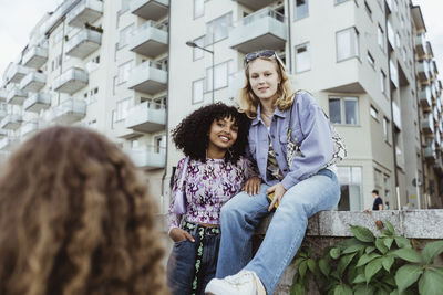 Portrait of smiling friends by retaining wall in city