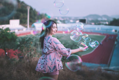 Woman walking amidst bubbles against sky