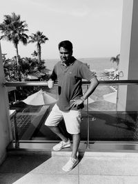 Portrait of young man standing by swimming pool against sky