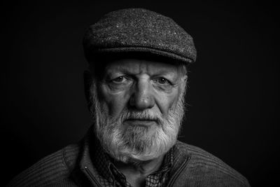 Portrait of old man wearing hat against black background