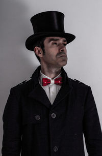 Mature man wearing coat and hat while standing against wall