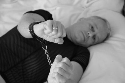 Portrait of mature man wearing handcuffs lying on bed