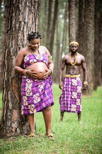 Man with pregnant wife standing against trees