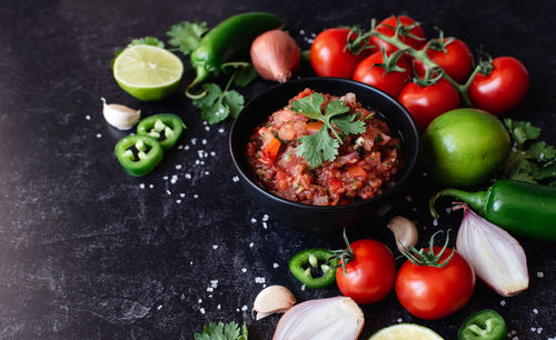 Bowl of fresh salsa with the ingredients and on black slate counter.