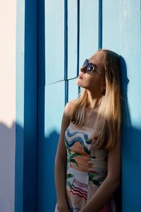 Portrait of young woman standing against blue wall