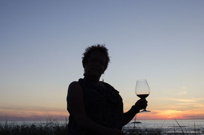 Silhouette woman holding umbrella against sky during sunset