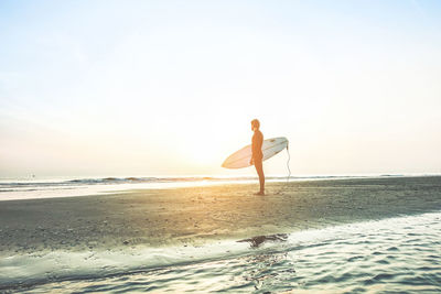 Full length of man with surfboard standing on beach against sky