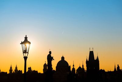 Silhouette gas light and buildings against sky during sunset