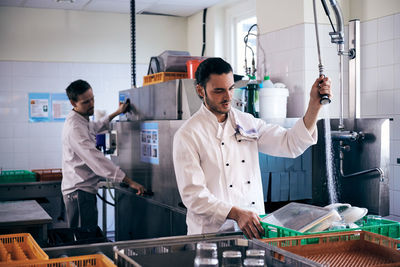 Chef spraying water on plates while colleague working in commercial kitchen