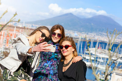 Smiling friends wearing sunglasses taking selfie with smart phone