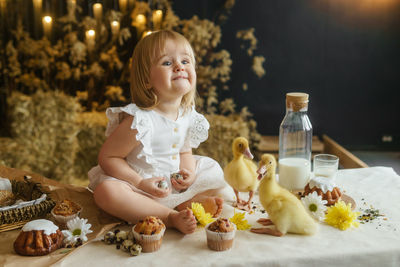 A little girl is sitting on the easter table and playing with cute fluffy ducklings. happy easter.