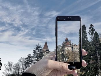 Person photographing with mobile phone against sky