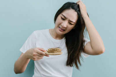 Worried woman holding brush with hair against blue background