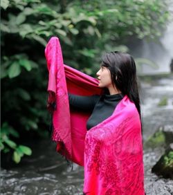 Side view of young woman standing against pink water