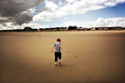 Rear view of boy standing on beach against sky