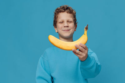 Portrait of woman holding banana against blue background