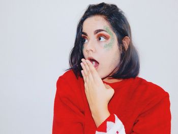 Surprised woman with glitter on face standing against white wall