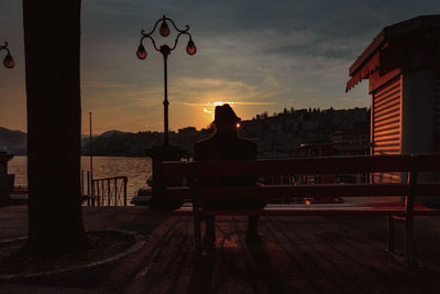 Silhouette person sitting on street against buildings in city during sunset
