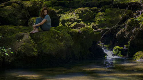Woman sitting on rock by stream
