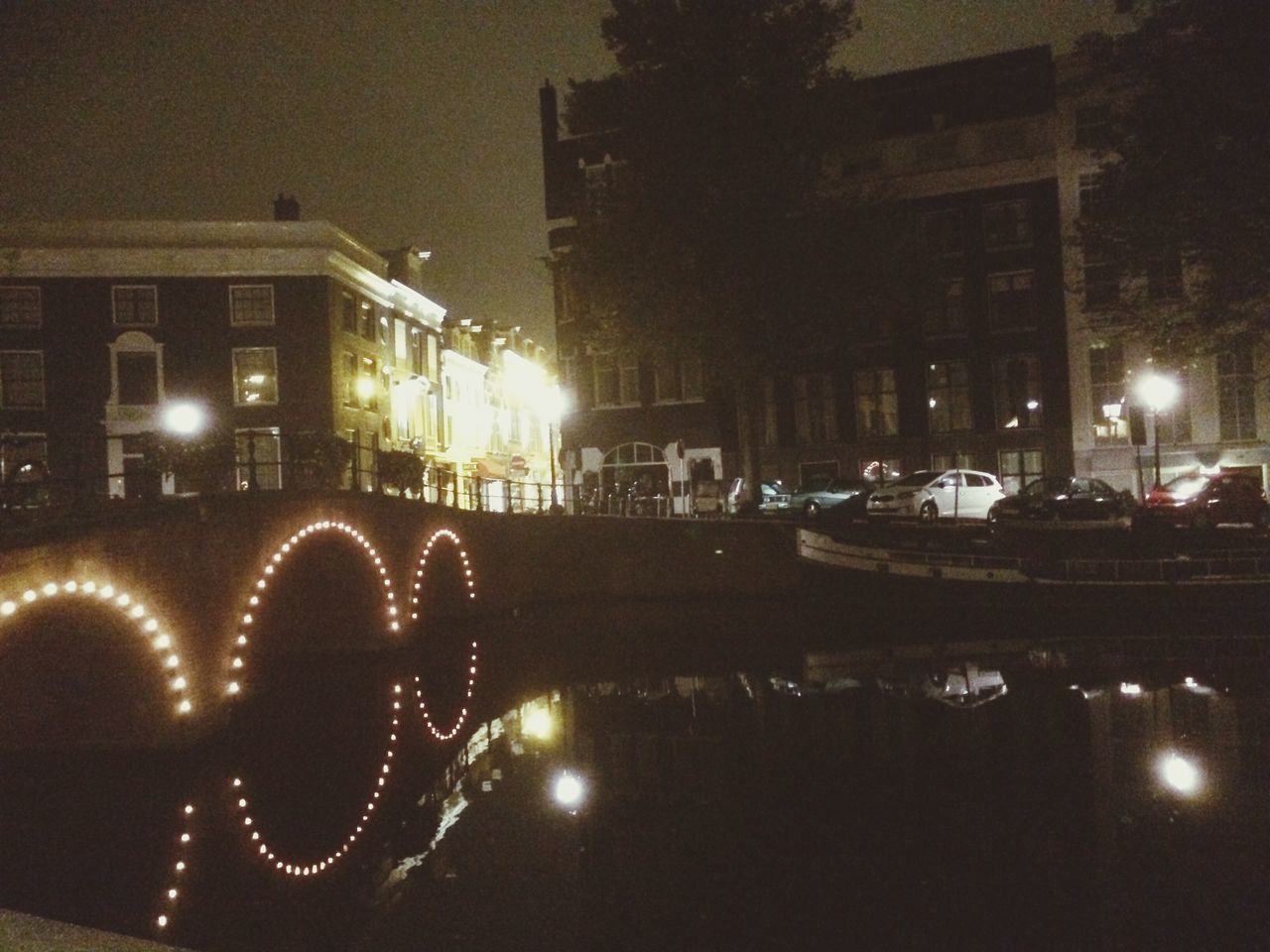 illuminated, night, building exterior, street light, built structure, architecture, transportation, water, reflection, mode of transport, city, lighting equipment, sky, river, street, nautical vessel, outdoors, dark, glowing, land vehicle